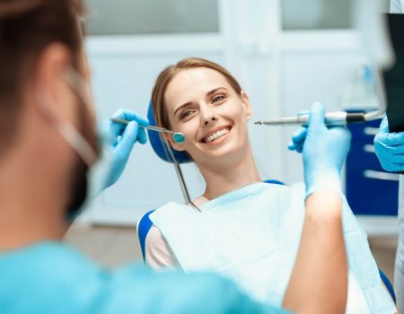 A young woman sits in a dental chair and smiles. Doctors bowed over her. They are going to treat her teeth. Happy patient and dentist concept.